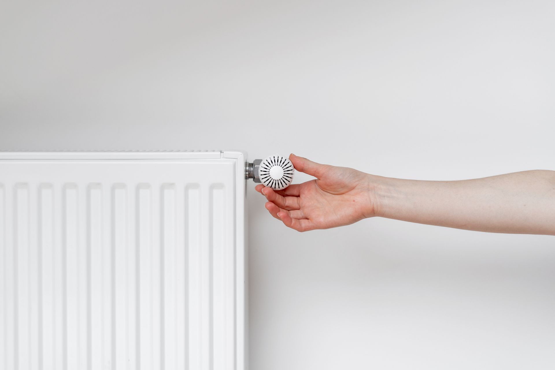 Une personne qui règle le thermostat d'un radiateur mural blanc.
