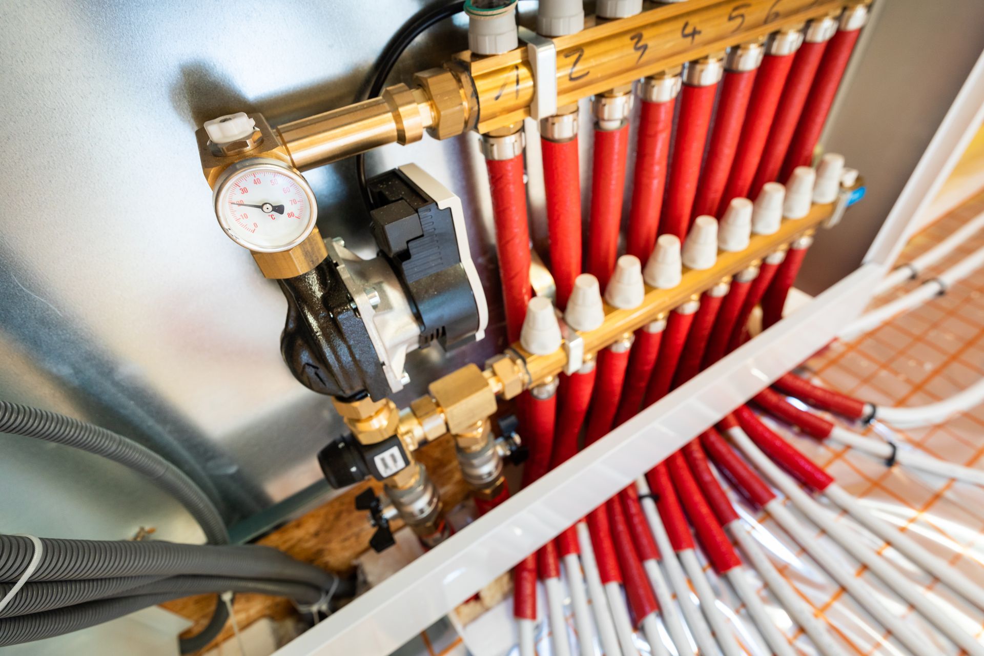 Un système de collecteur en laiton pour chauffage au sol radiant avec raccords de tuyauterie rouges et blancs et un manomètre.