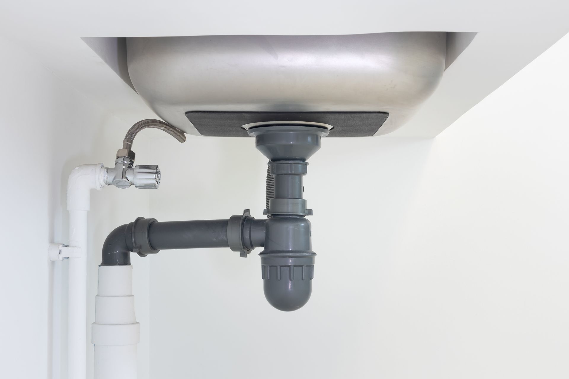 Un système d'évacuation d'évier de cuisine comprenant un siphon en plastique gris et des tuyaux reliés à une cuve d'évier en acier inoxydable.