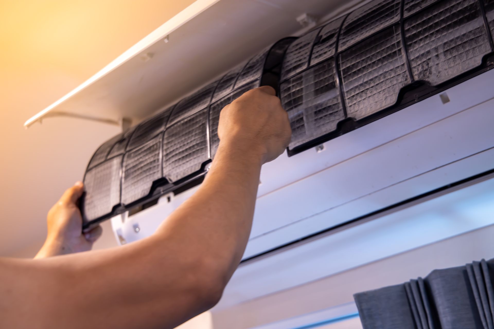 Une personne retire le filtre à mailles d'un climatiseur mural intérieur pour le nettoyer.