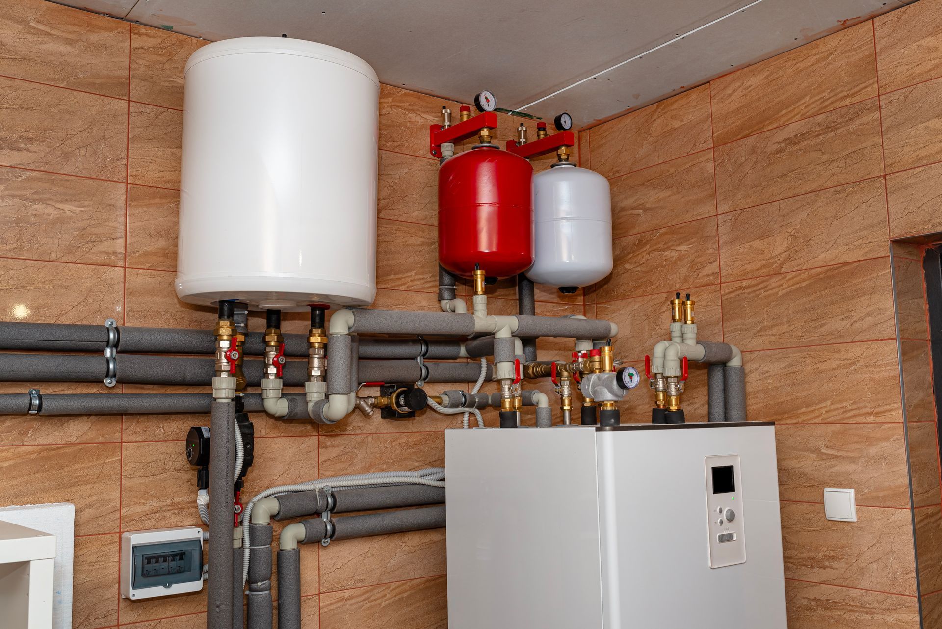 Installation d'un système de chauffage comprenant un grand réservoir blanc, des vases d'expansion rouges et blancs et des tuyaux isolés fixés au mur.