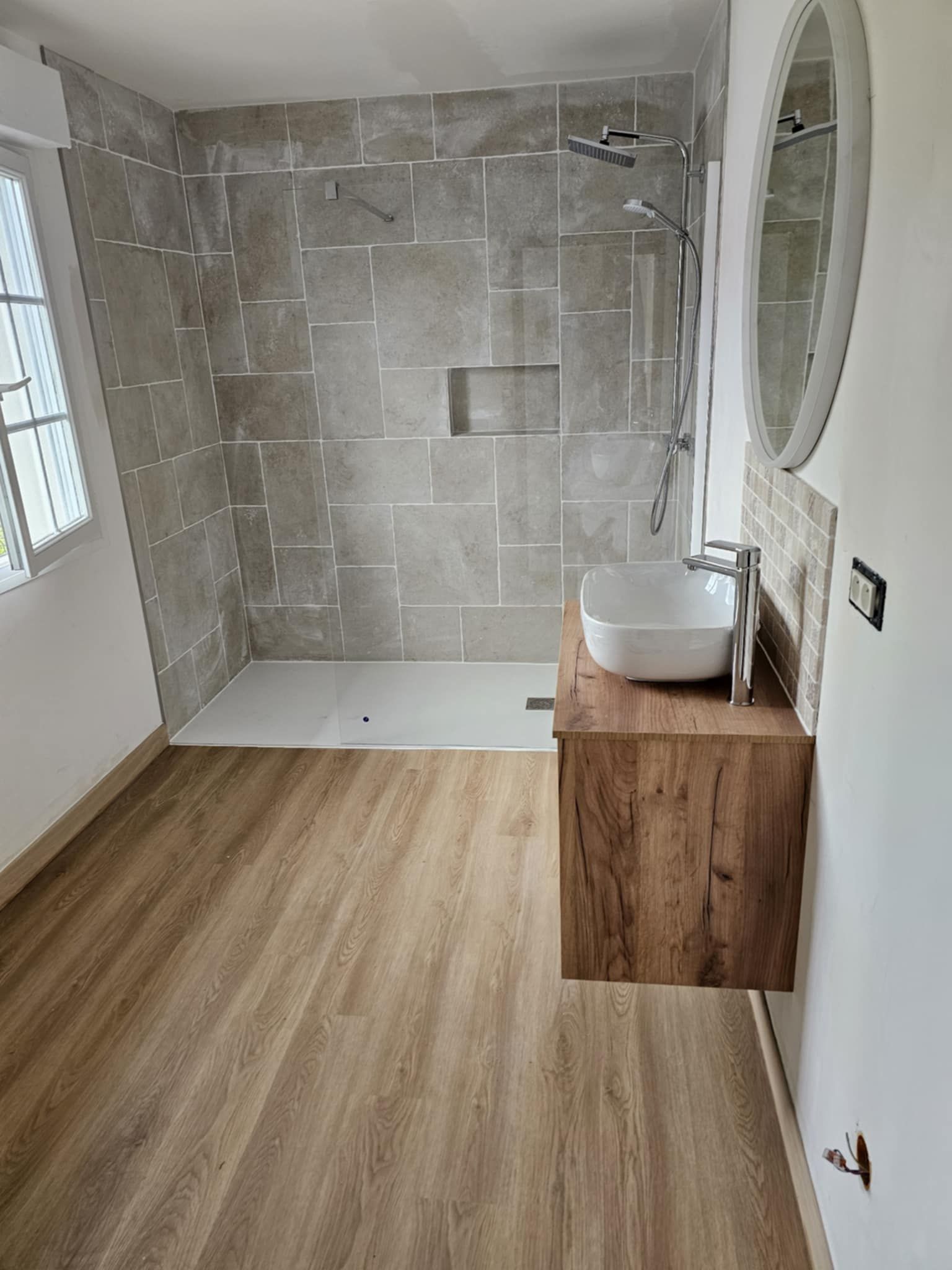 Une main gantée utilise une clé à pipe rouge pour ajuster les tuyaux de plomberie chromés sous un lavabo de salle de bains.