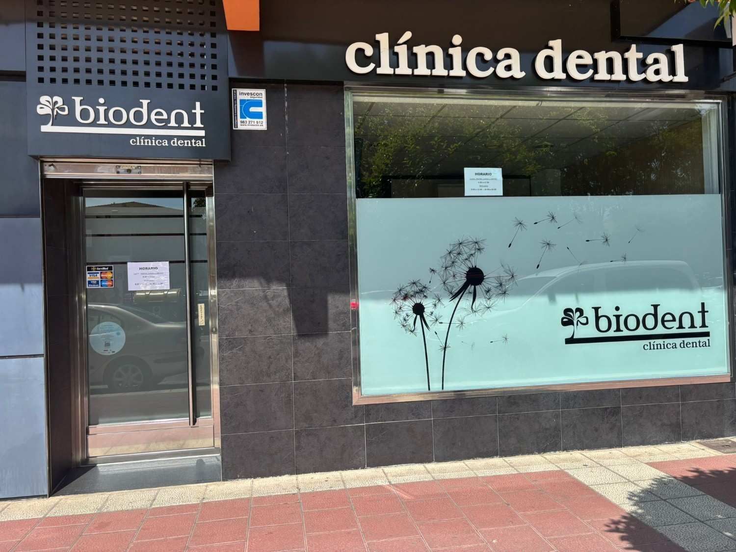 Fachada de la clínica dental Biodent con puerta de cristal, fachada negra y letrero en la ventana con vidrio esmerilado.