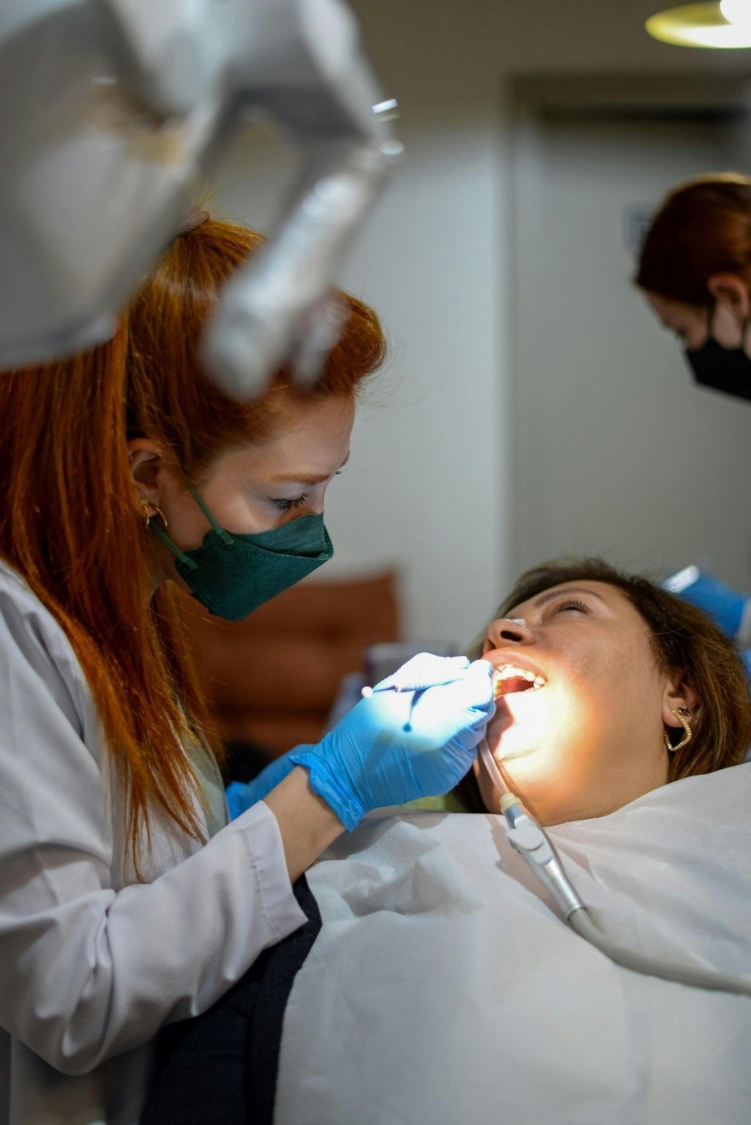 Dentista y asistente examinando la boca abierta de un paciente con luz brillante en una clínica dental.