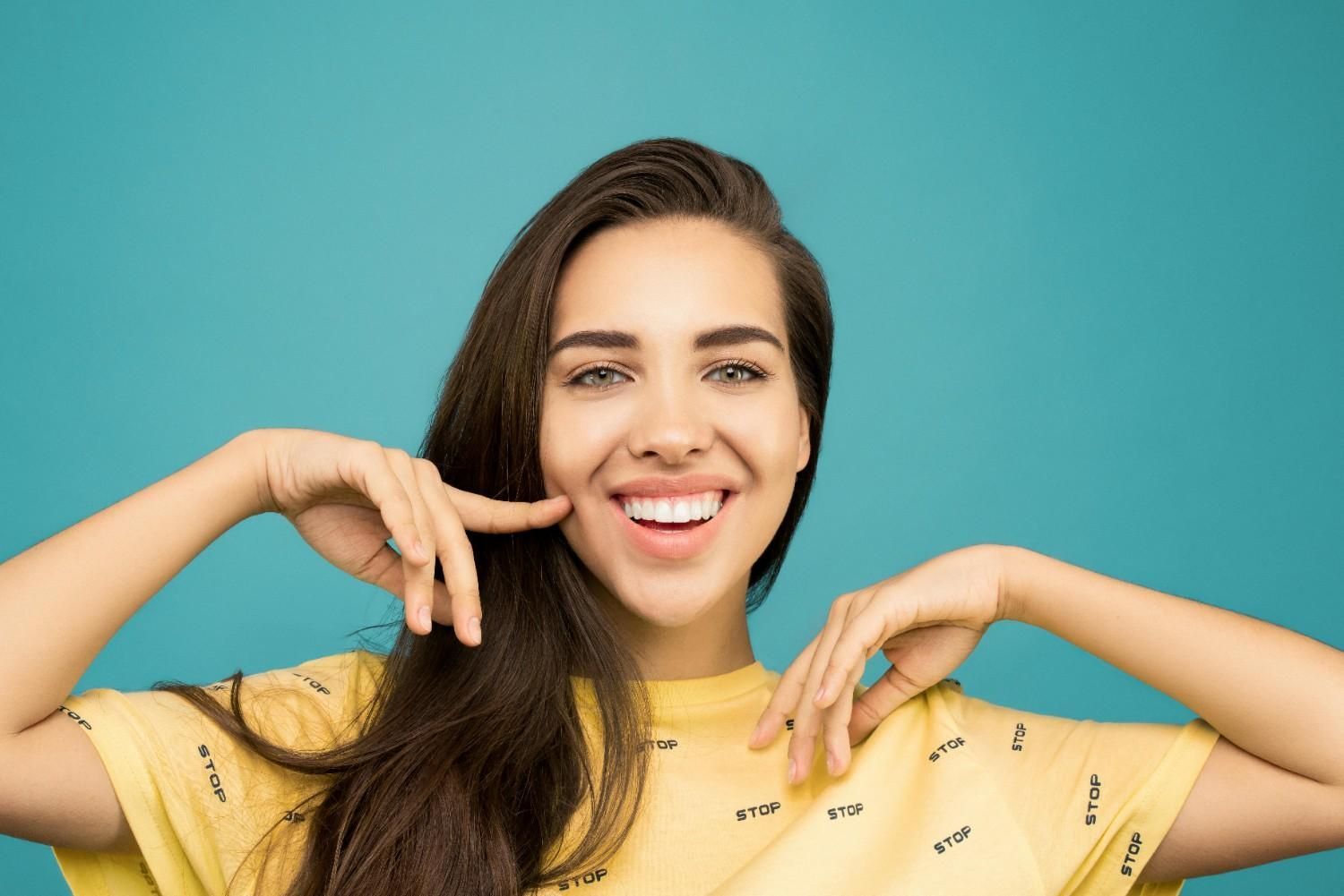 Mujer sonriente con camisa amarilla posando sobre un fondo turquesa.