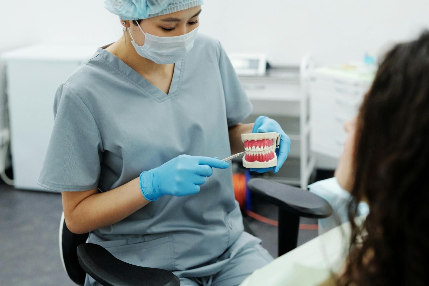 Dentista con bata azul mostrando un modelo dental a un paciente en una clínica.