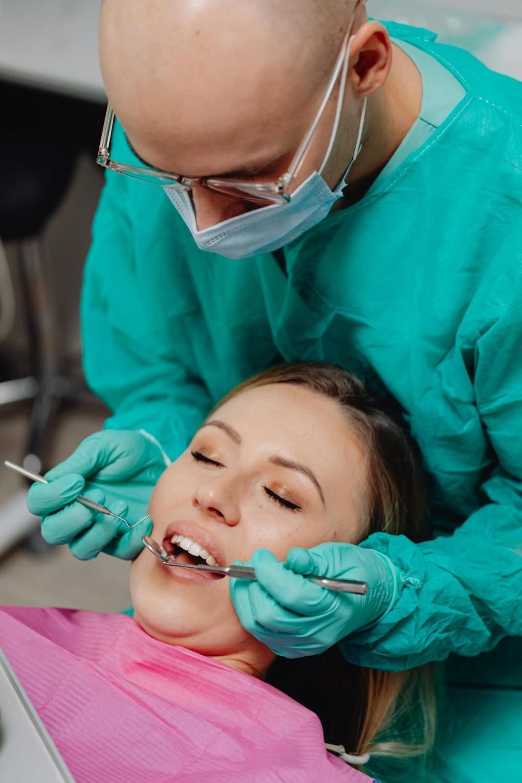 Dentista examinando a un paciente sonriente en el sillón dental, vistiendo bata y guantes de color turquesa.