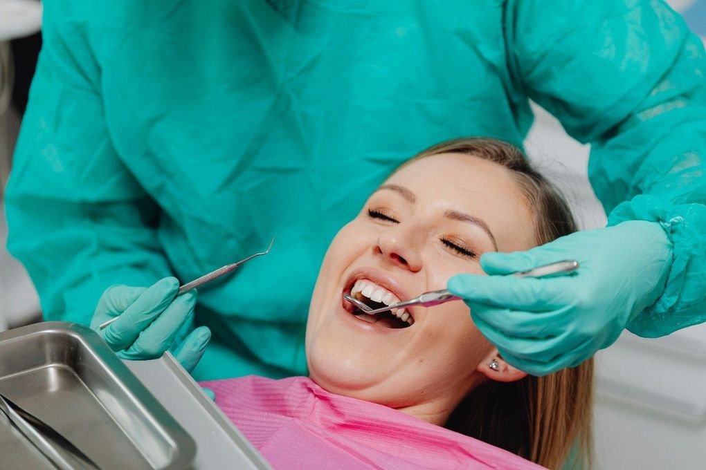 Un dentista utiliza un espejo y un instrumento para examinar a un paciente sonriente en el sillón dental.