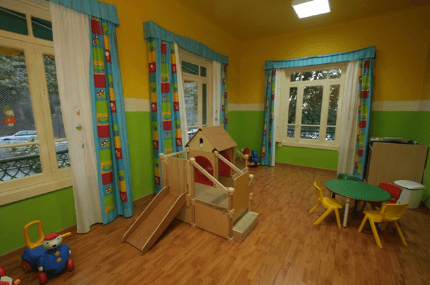 Sala de juegos con estructura de madera, mesa pequeña y ventanas con cortinas de colores.