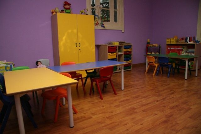 Un aula preescolar de colores brillantes con mesas y sillas, un armario de almacenamiento y juguetes.