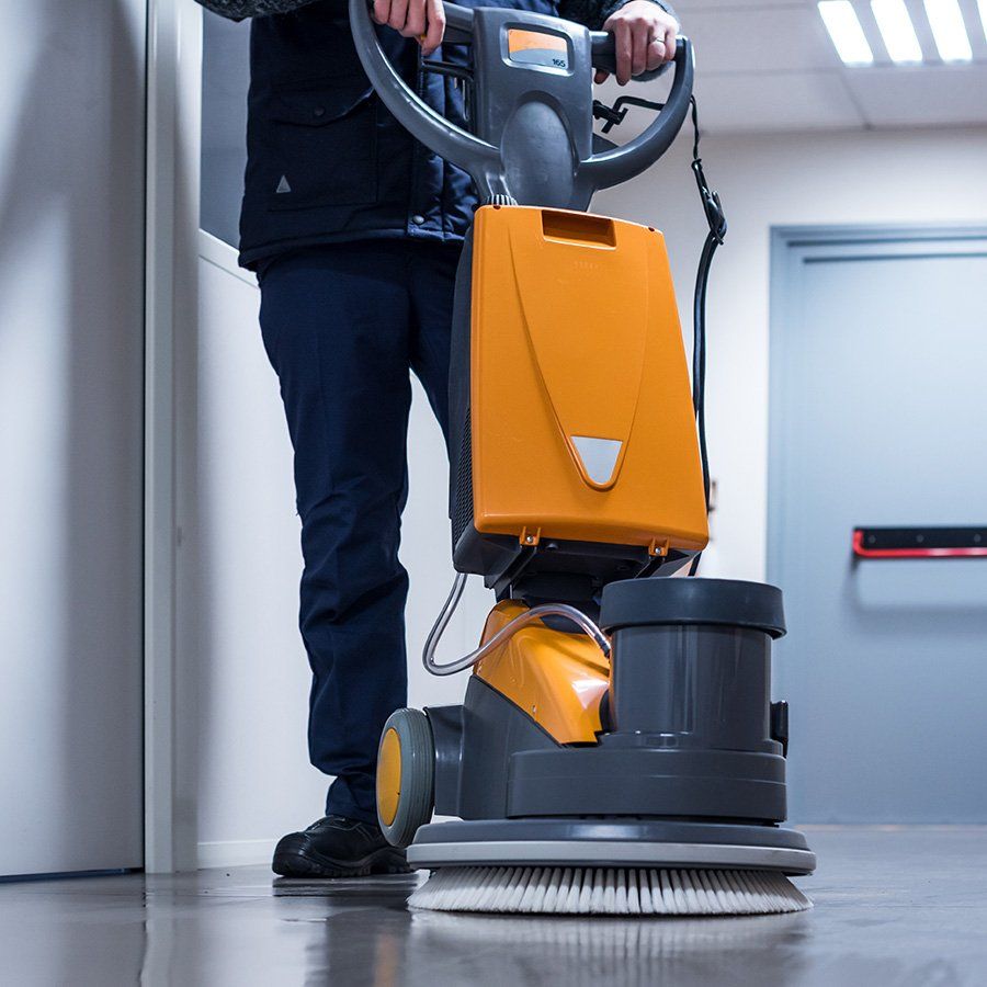 Un employé qui nettoie le sol avec une machine orange