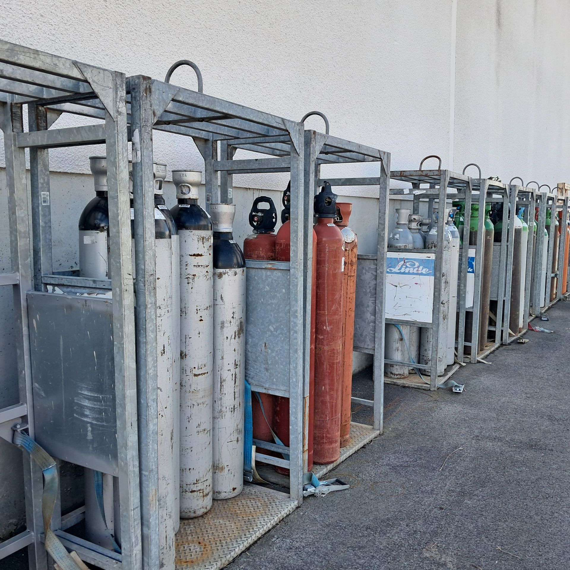 Bouteilles de gaz de couleurs variées, rangées dans des cages métalliques contre un mur