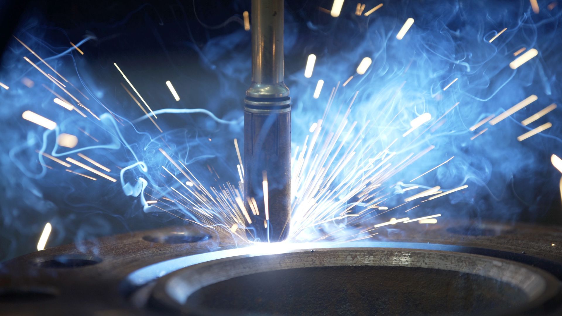 Machine à souder en action, créant des étincelles et une lumière bleue brillante sur le métal.
