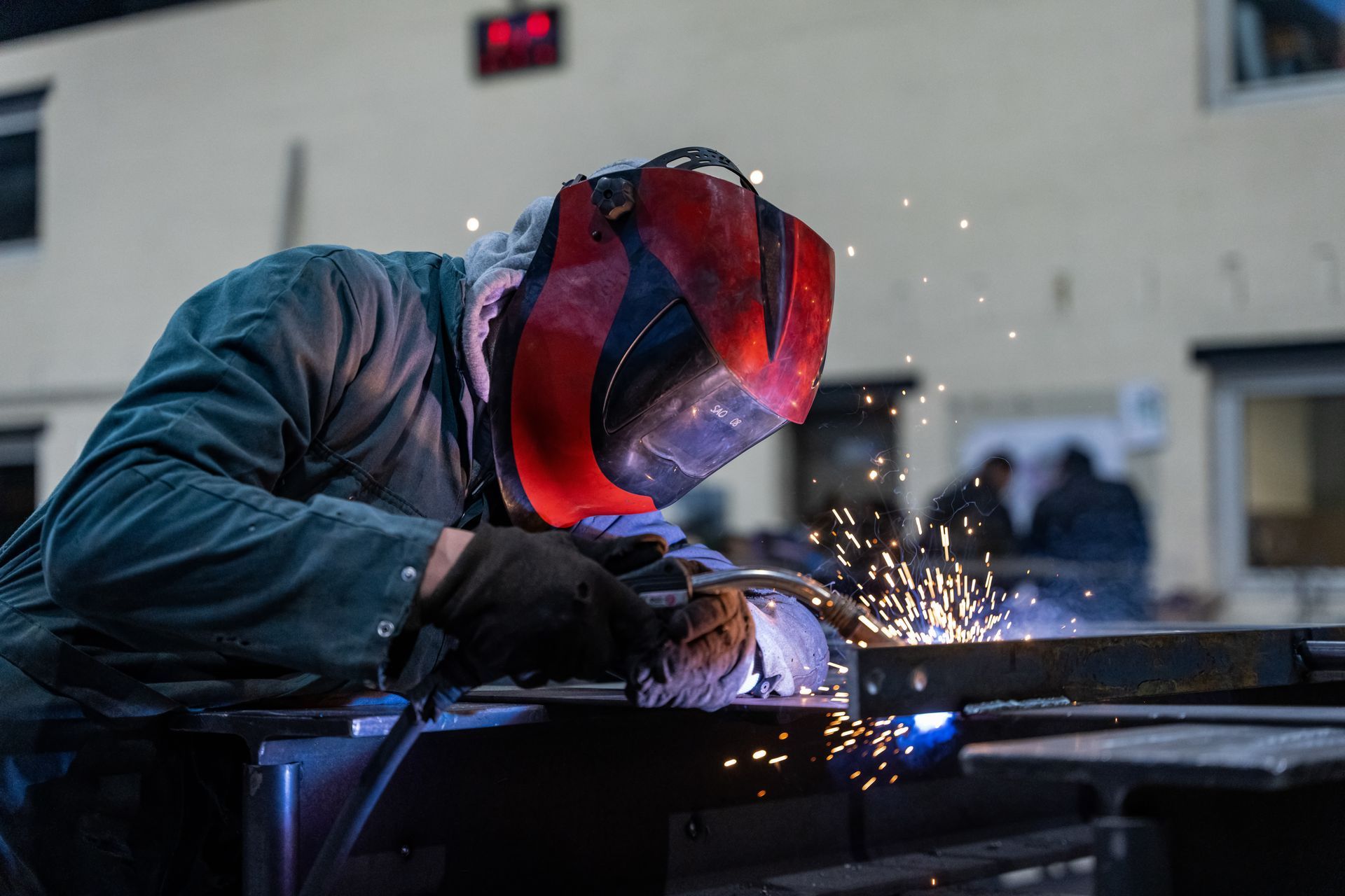 Soudeur portant un casque rouge, soudant du métal avec des étincelles volant autour.