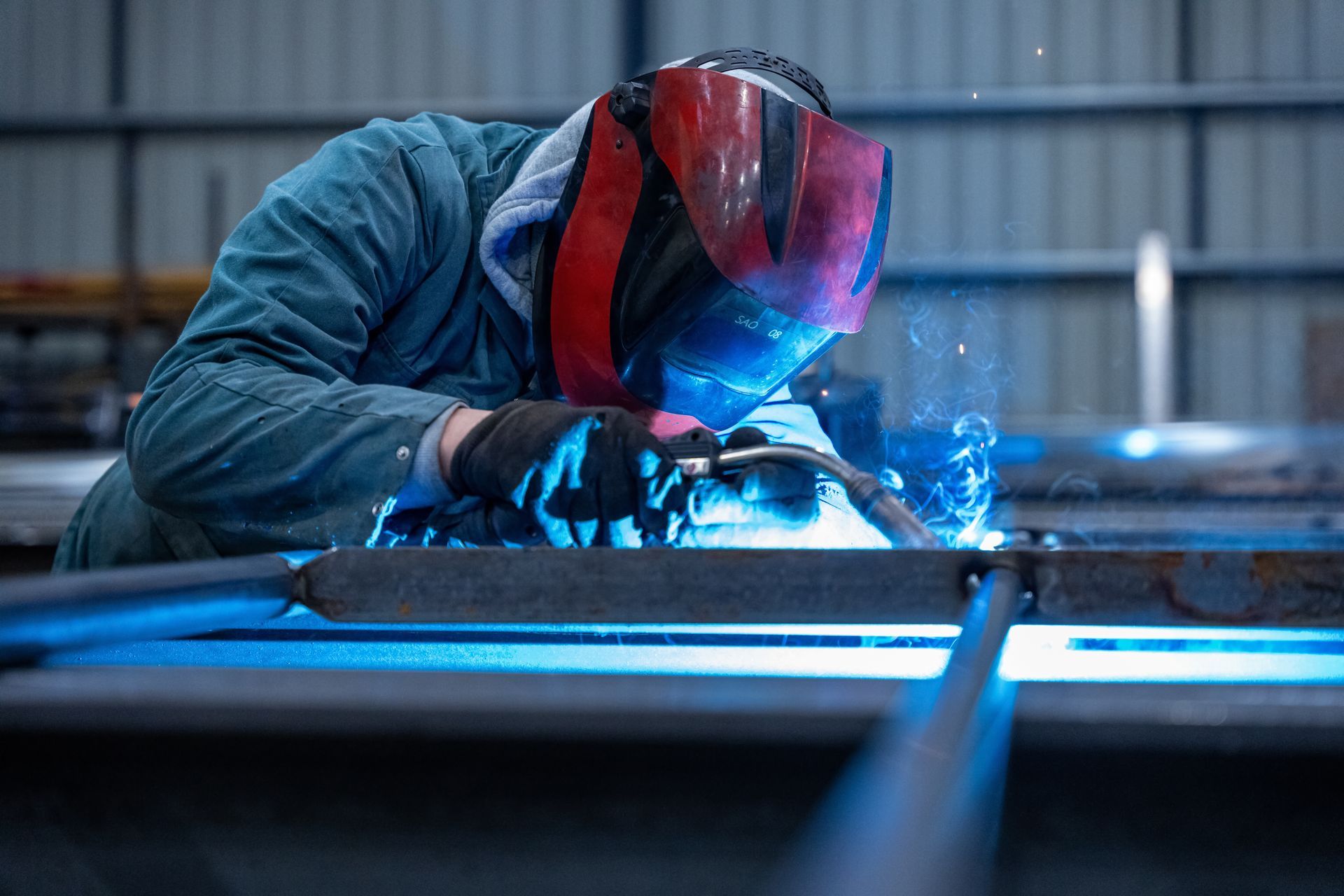 Soudeur portant un casque rouge, travaillant avec du métal.