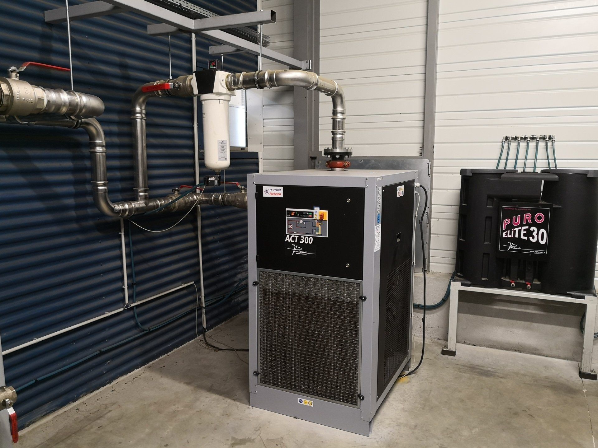 Compresseur noir avec la tuyauterie connectée et des bouteilles sur un rack.