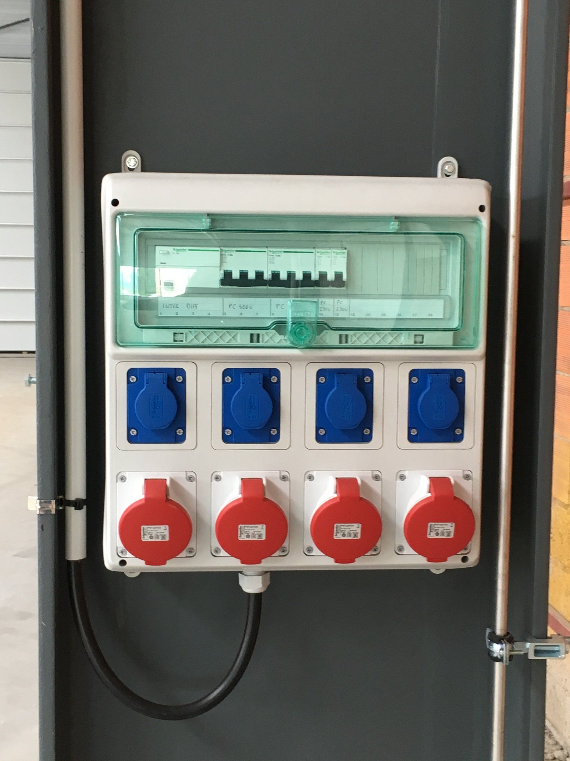Panneau électrique avec prises de courant bleues et rouges sur un mur gris.