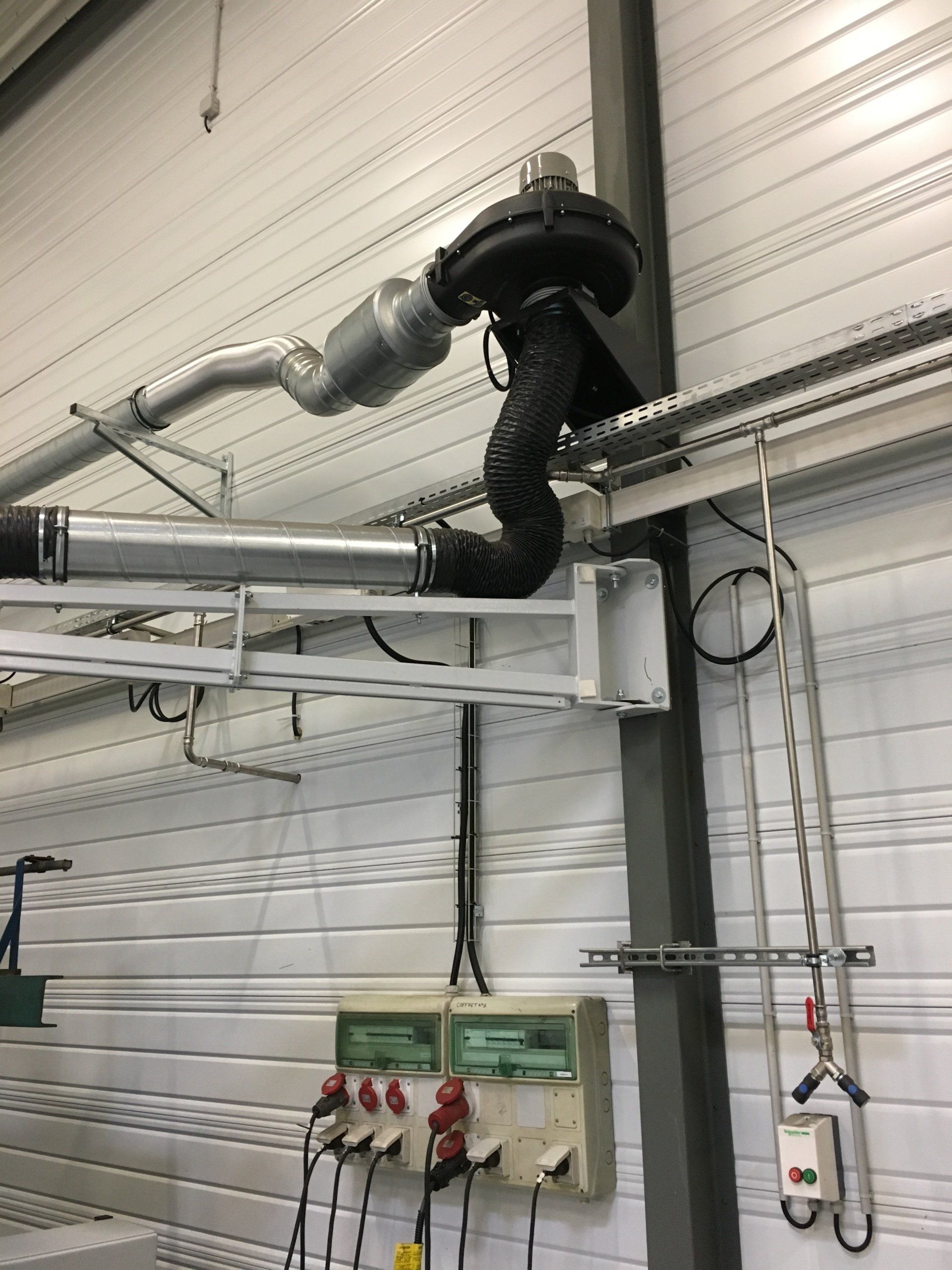 Système d'échappement et panneau électrique montés sur un mur de bâtiment industriel blanc.