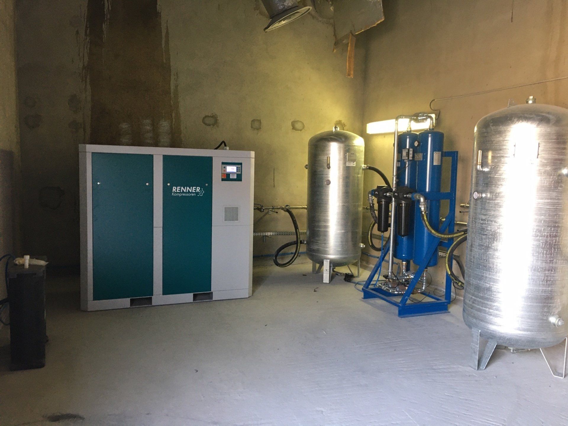 Local technique avec un grand compresseur bleu et gris, des réservoirs argentés et un système de traitement d'air bleu.
