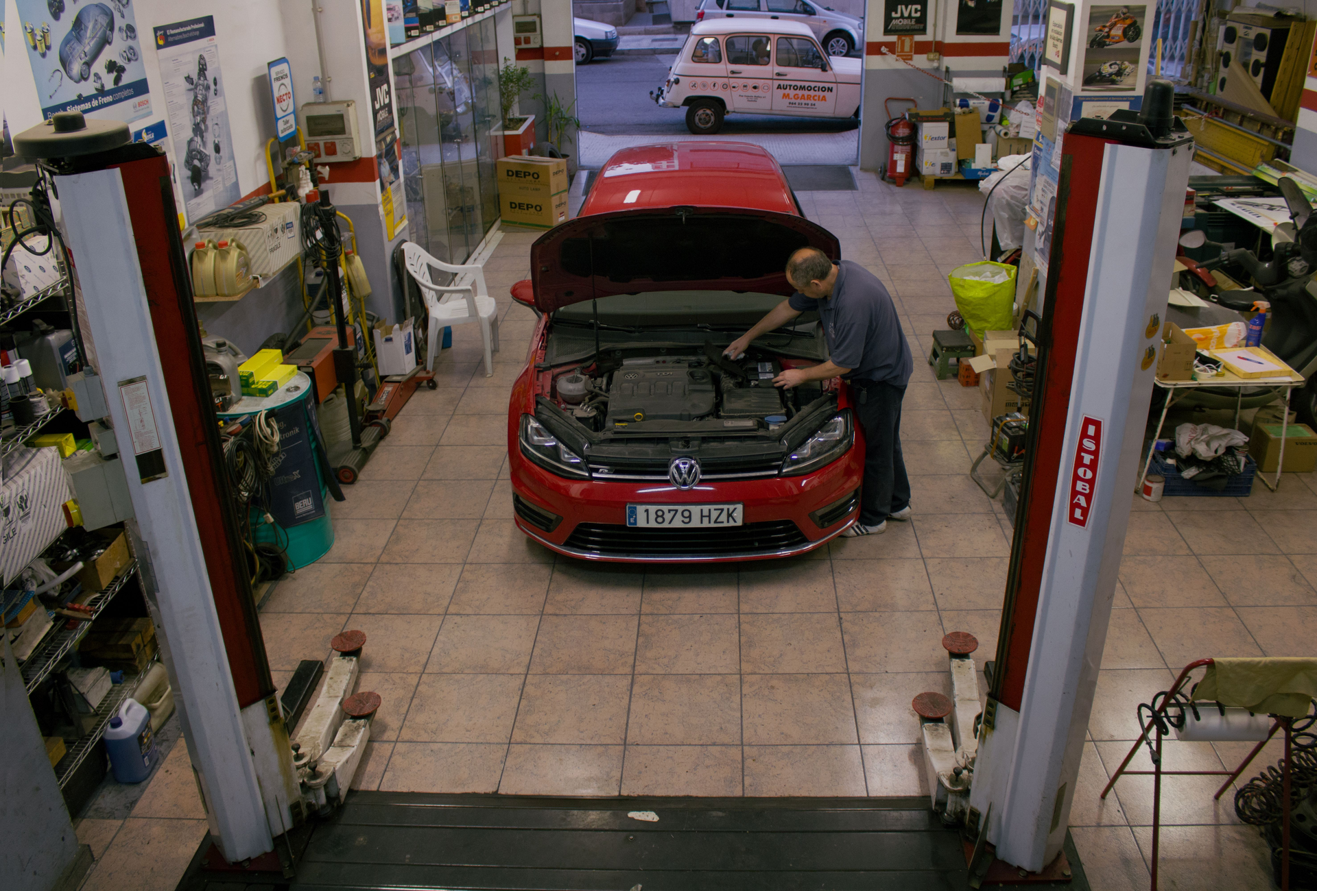 Un mecánico trabaja en un coche rojo en un taller. Está rodeado de herramientas y equipo.