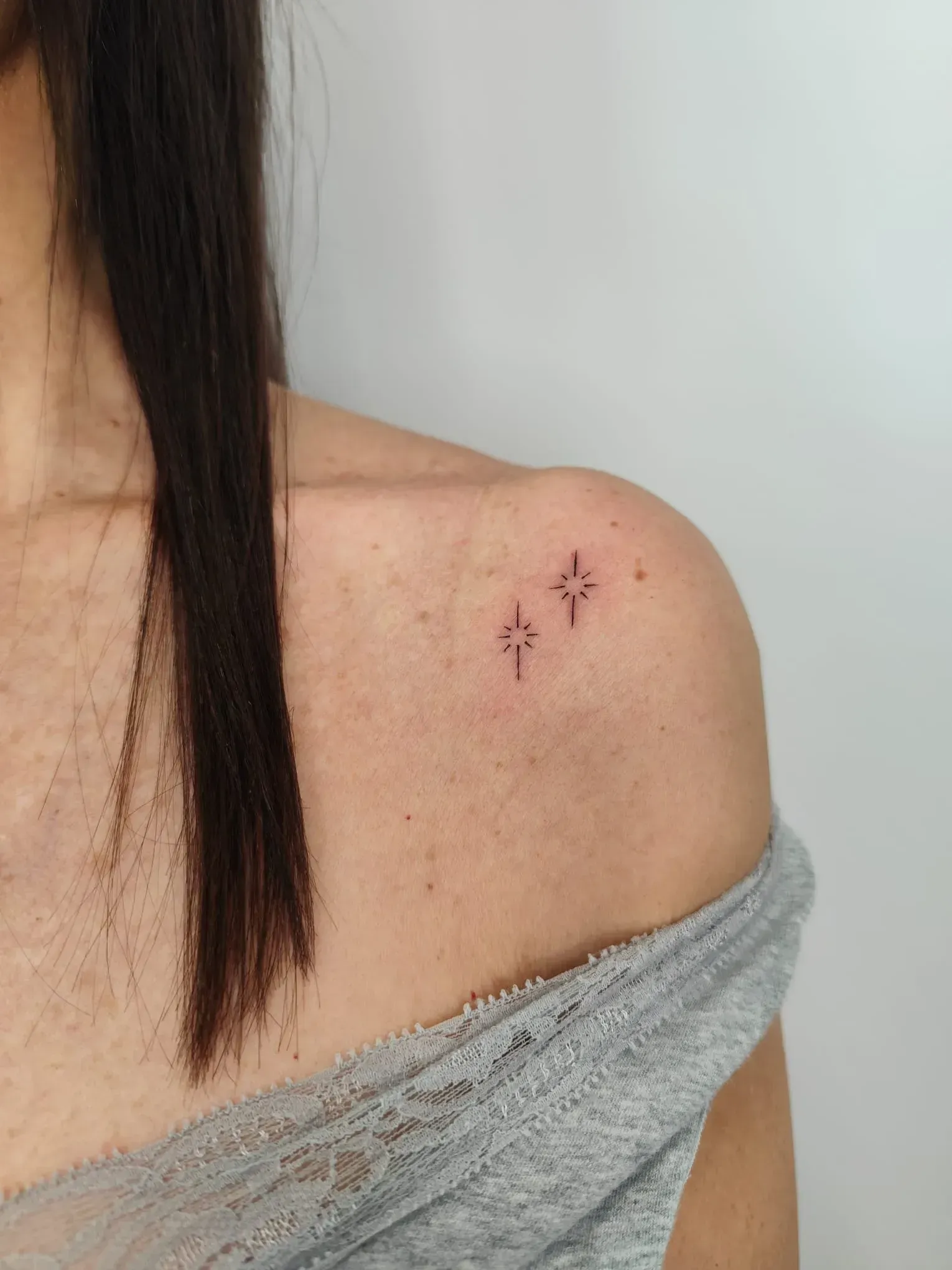 Hombro con tres pequeñas marcas rojas parecidas a tatuajes cerca de la clavícula, lleva una blusa gris sin hombros.