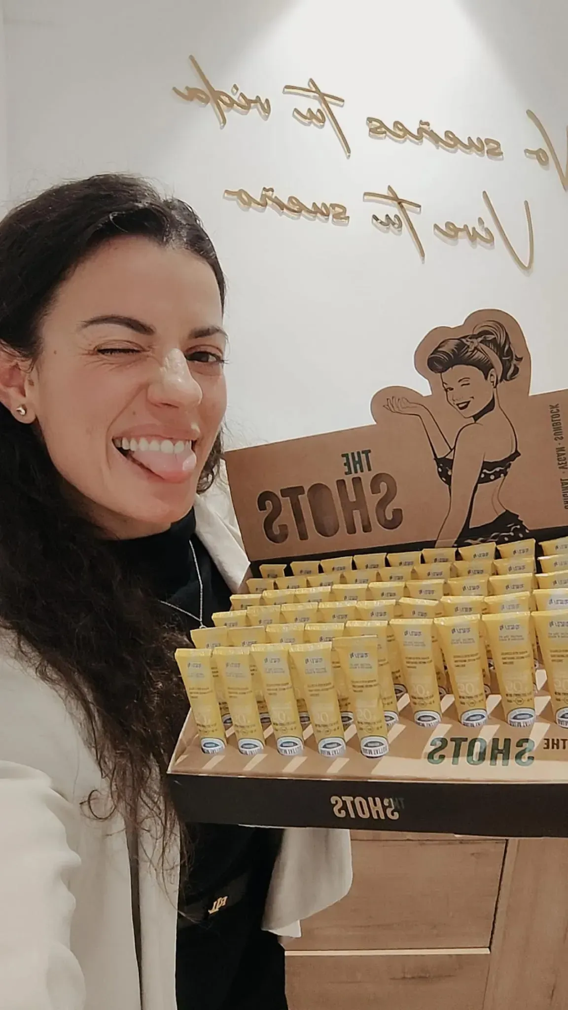 Una mujer sonríe junto a una vitrina de postres con dulces envueltos en papel dorado.