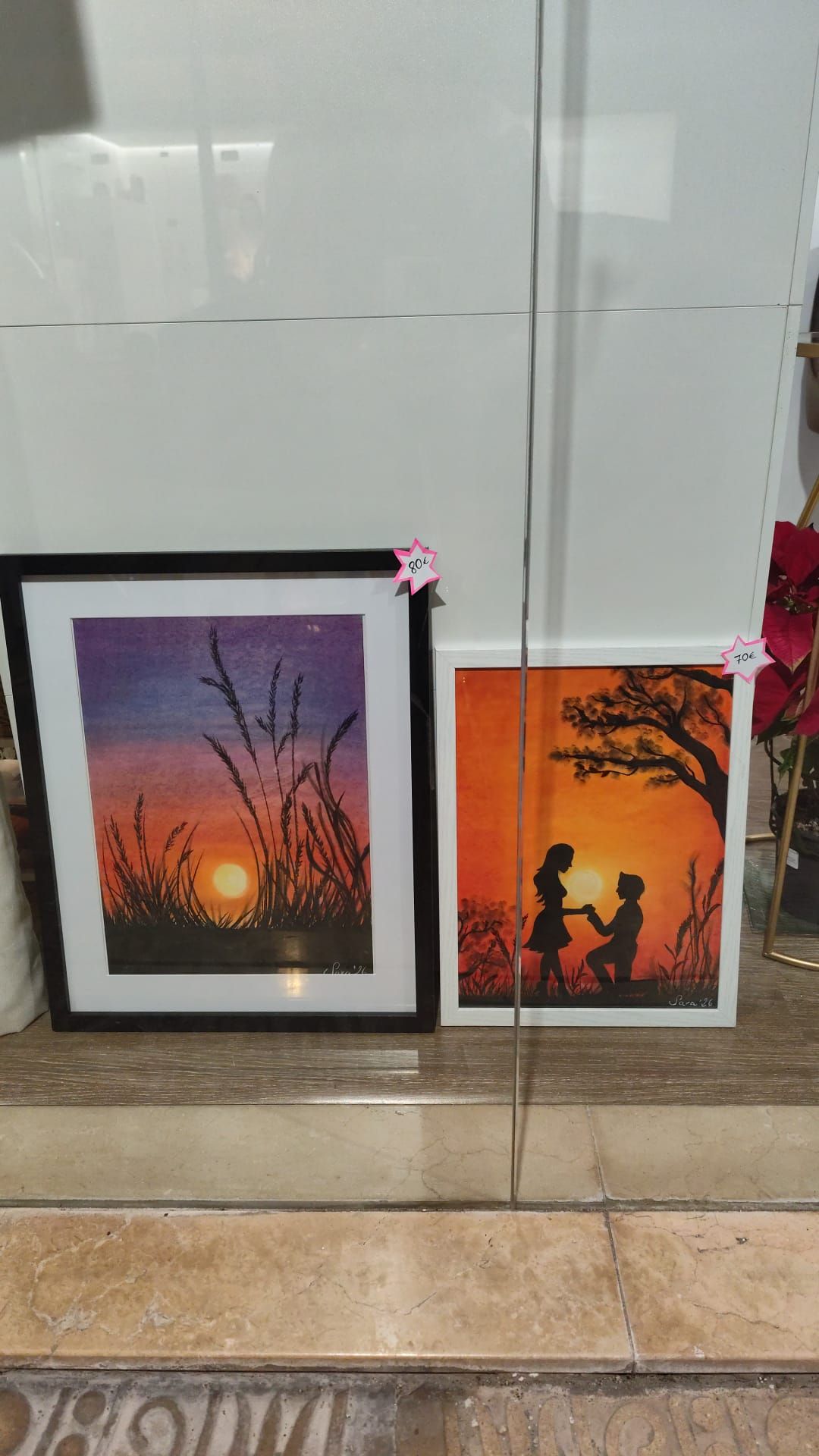 Dos obras de arte enmarcadas con siluetas de puestas de sol apoyadas contra una pared sobre un suelo de baldosas.