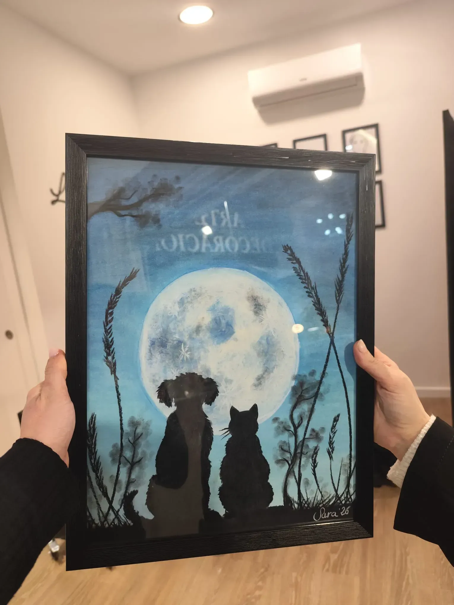 Cuadro enmarcado con imágenes de perros y gatos a la luz de la luna, expuesto en una habitación .