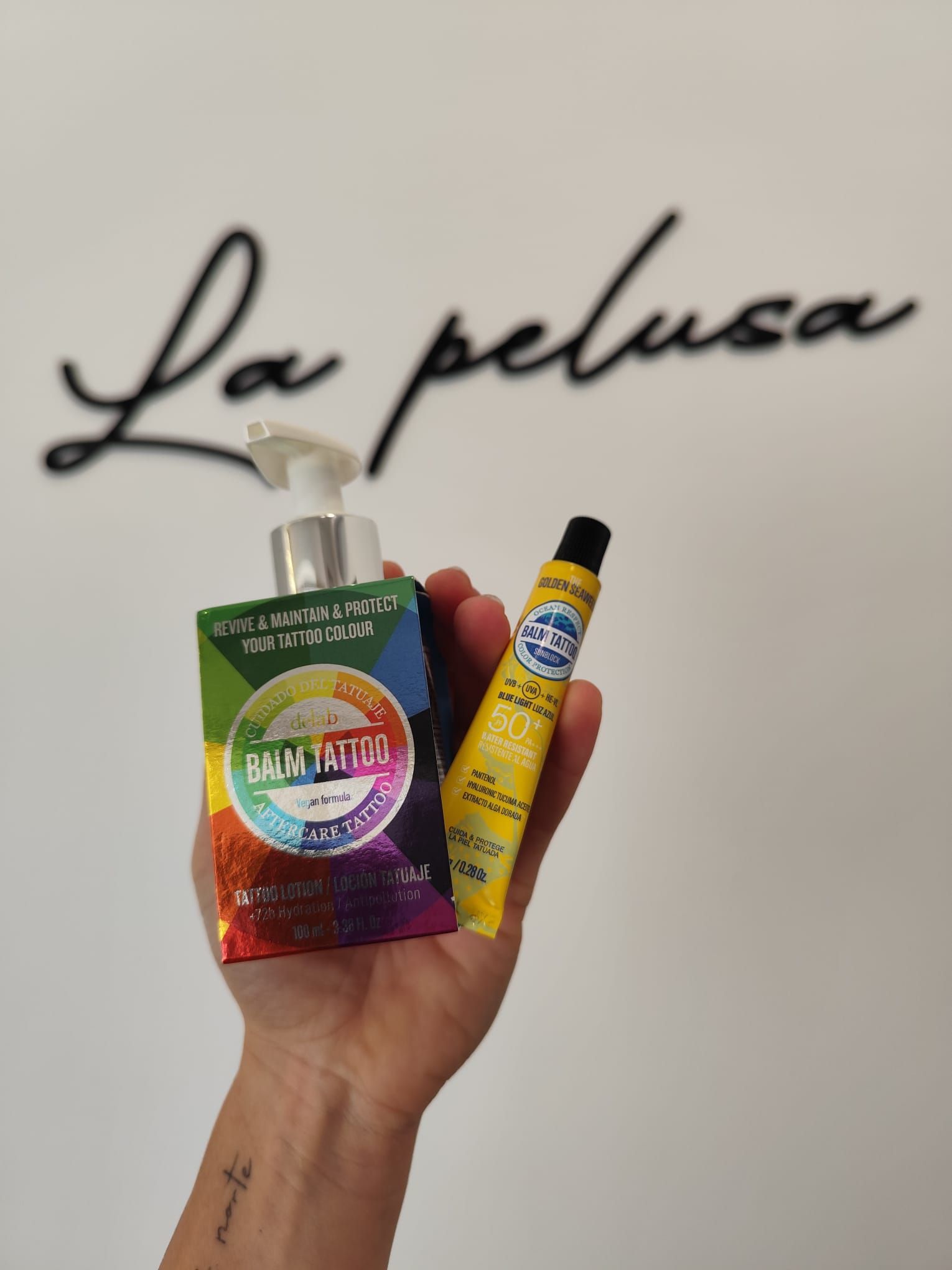 Mano sosteniendo un colorido set de productos de belleza contra una pared con la inscripción “La pelusa”.
