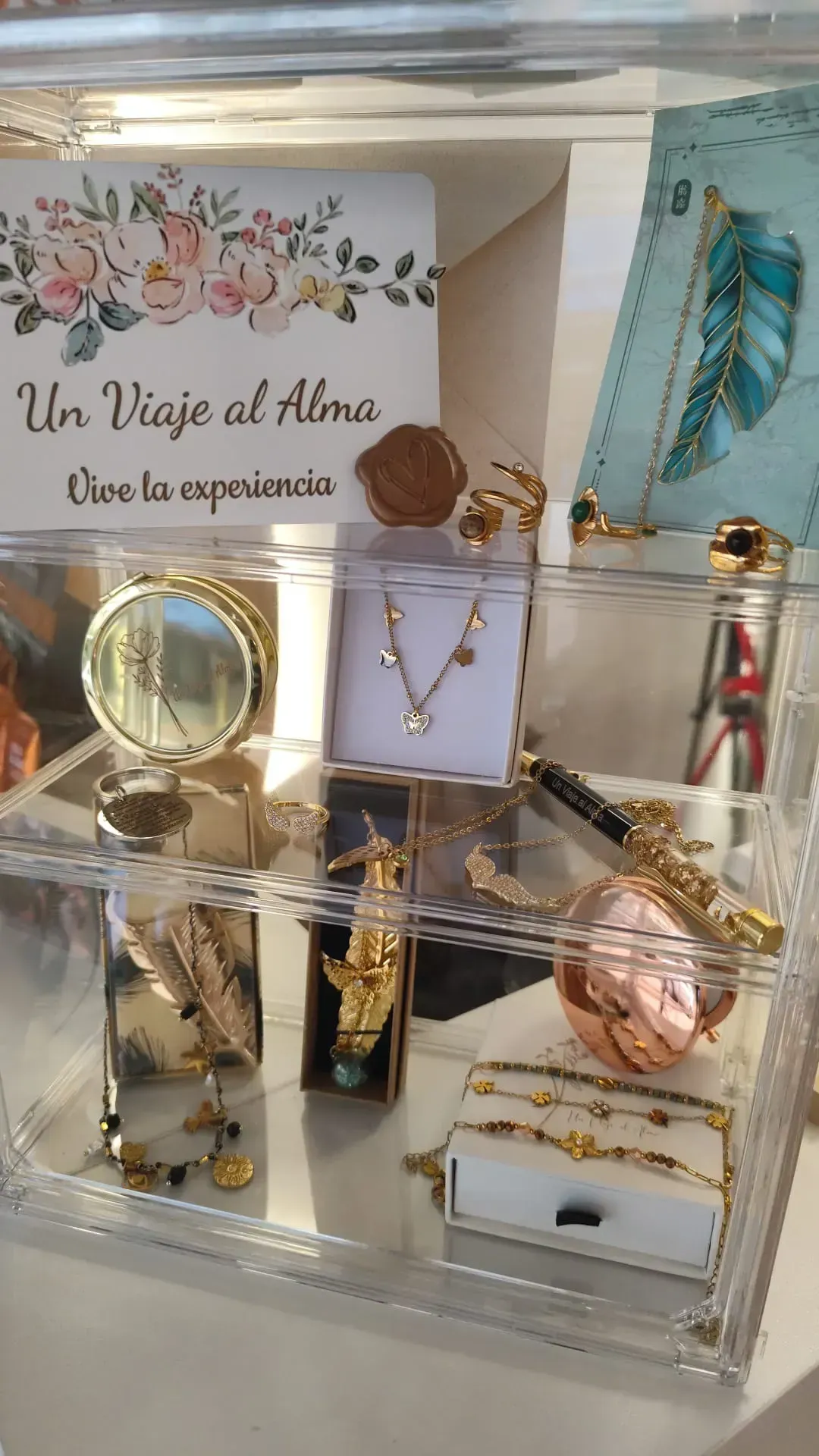 Una vitrina transparente con joyas de oro y oro rosa y un letrero floral que dice “Un Viaje al Alma”.