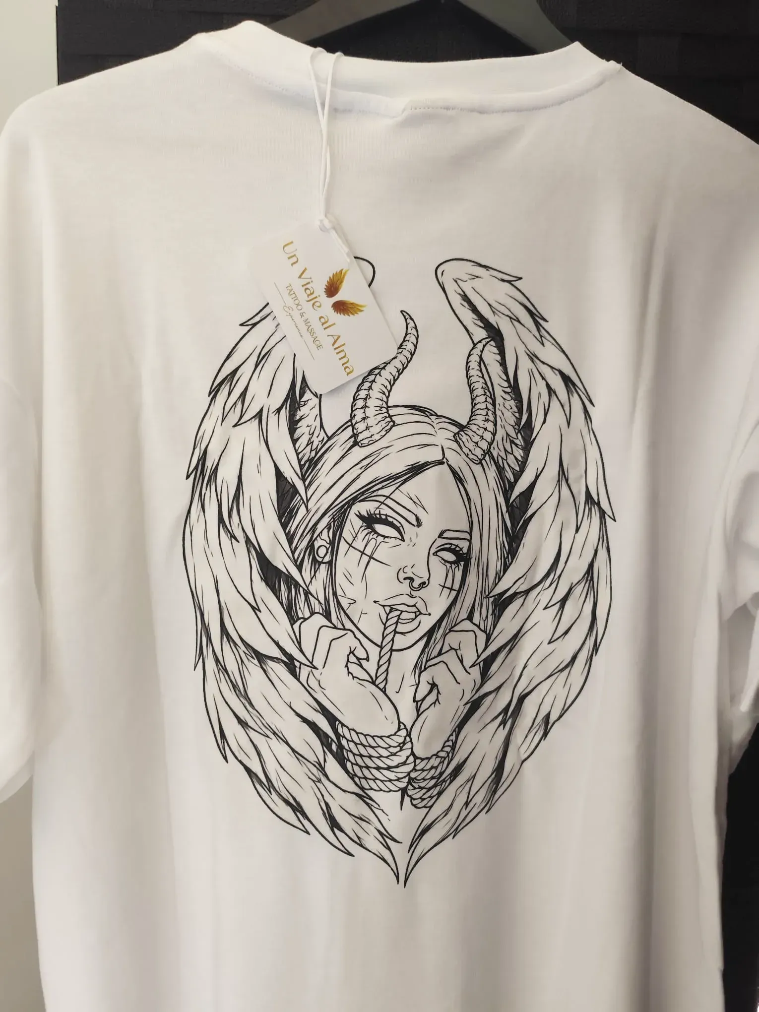 Camiseta blanca con una ilustración de un ángel en blanco y negro en la espalda.