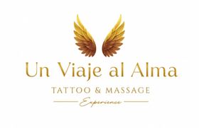 Logotipo de tatuaje y masaje dorado con la inscripci&oacute;n &ldquo;Un Viaje al Alma&rdquo; y alas sobre fondo blanco.