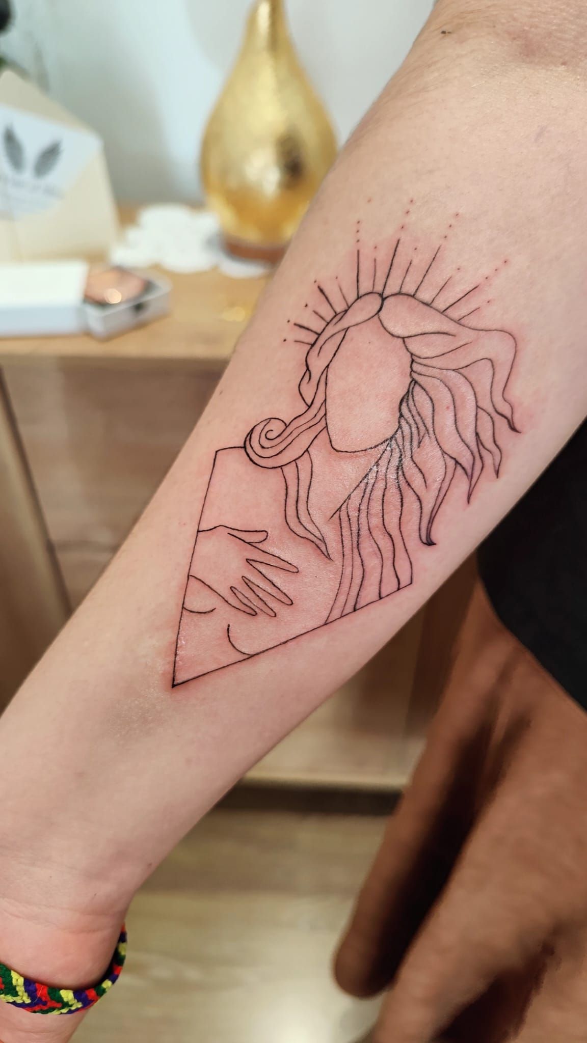 Antebrazo con un tatuaje de líneas negras de una flor y un diseño de rayos de sol.