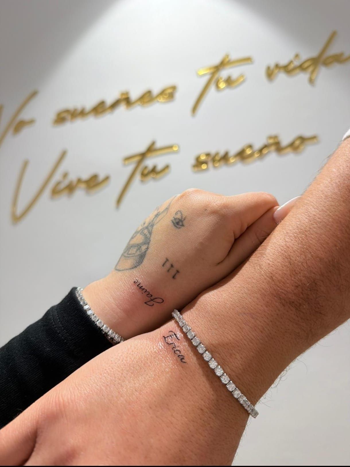 Dos manos entrelazadas, una con una pulsera de plata, con texto en letra cursiva dorada en el fondo.