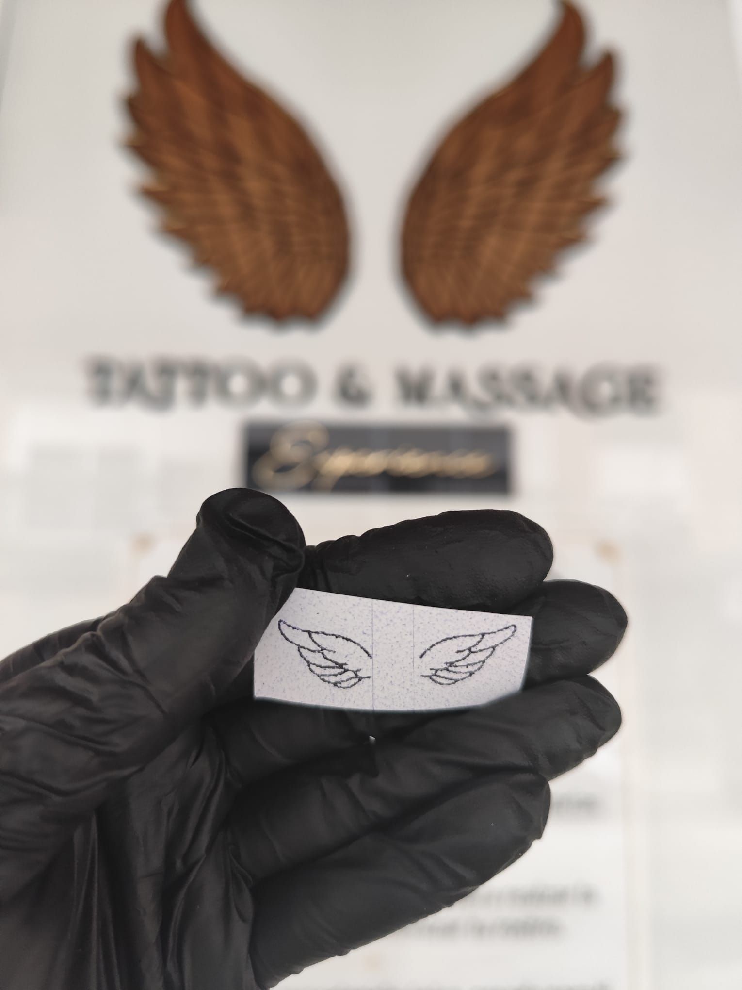 Mano enguantada de negro sosteniendo una pulsera blanca con pequeños tatuajes de plumas.