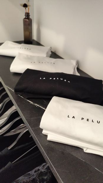 Prendas de CA PELUCI en blanco y negro dobladas y expuestas en un estante con un jarrón al fondo.
