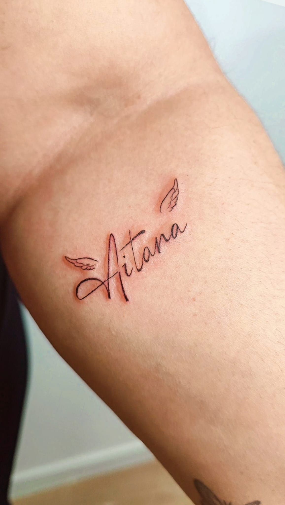 Primer plano de un antebrazo con un pequeño tatuaje de mariposa en letra cursiva cerca del codo.