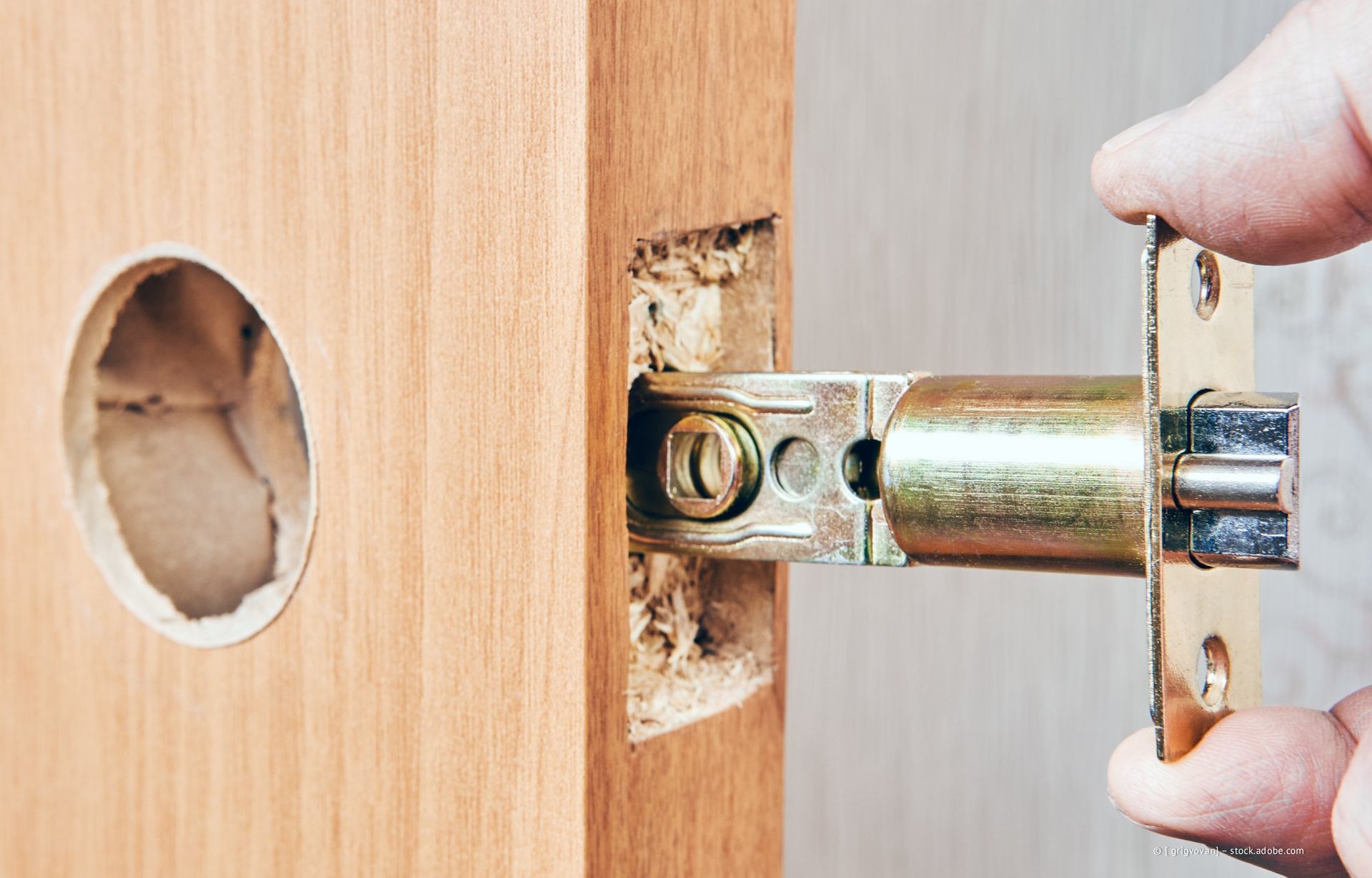 Eine Hand installiert einen Türriegel an einem hölzernen Türrahmen.