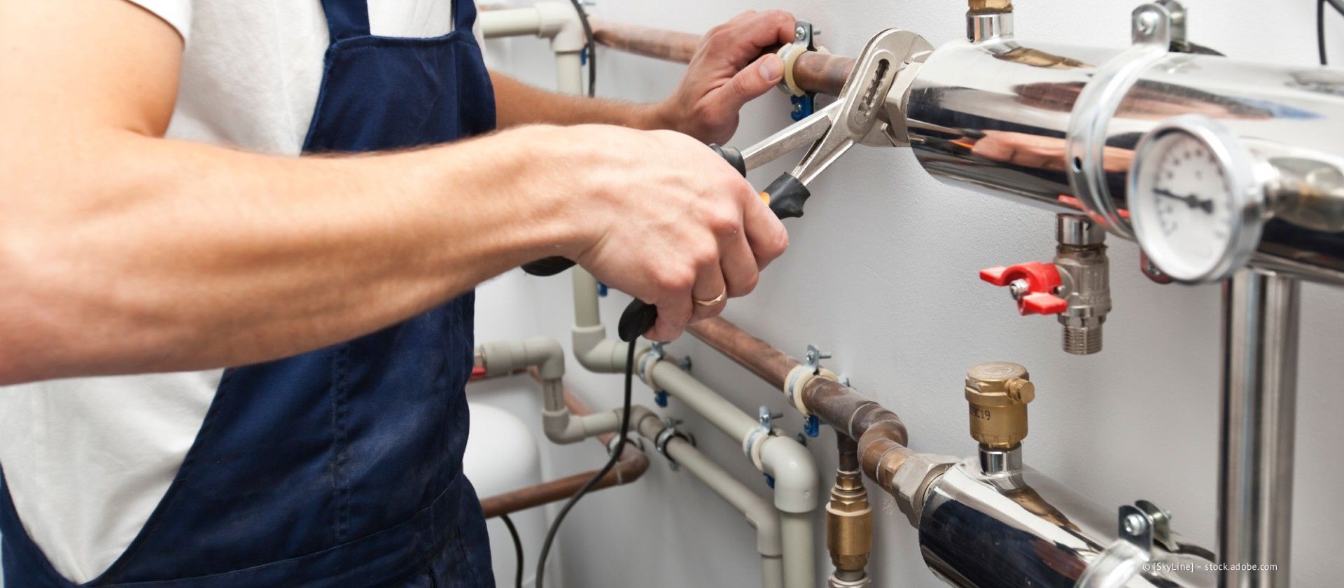 Ein Techniker zieht in einer Werkstatt Rohre an Industriemaschinen mit Schraubenschlüsseln fest.