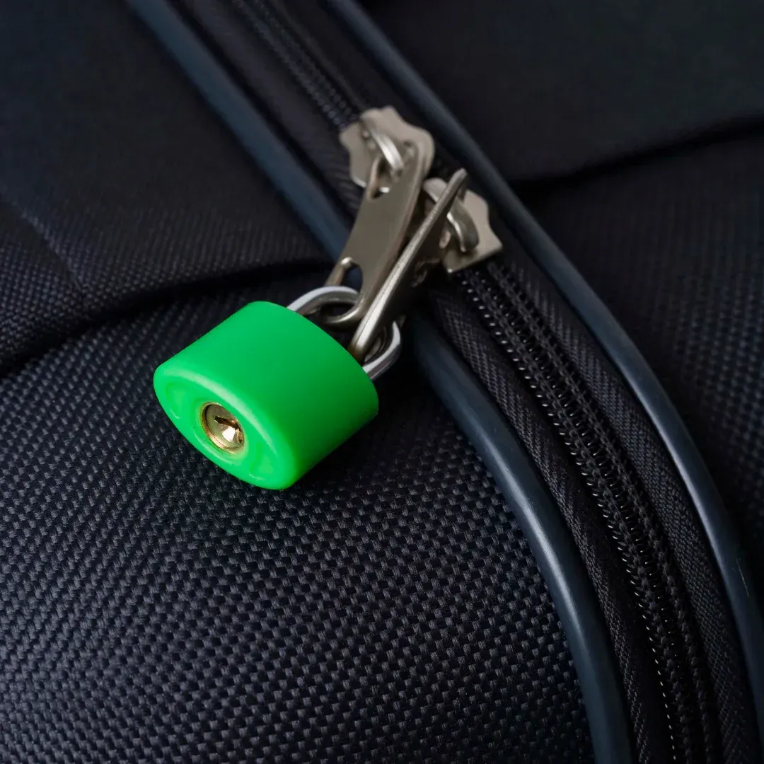 Un cadenas vert vif sécurise les tirettes métalliques de la fermeture éclair d'une valise noire texturée.