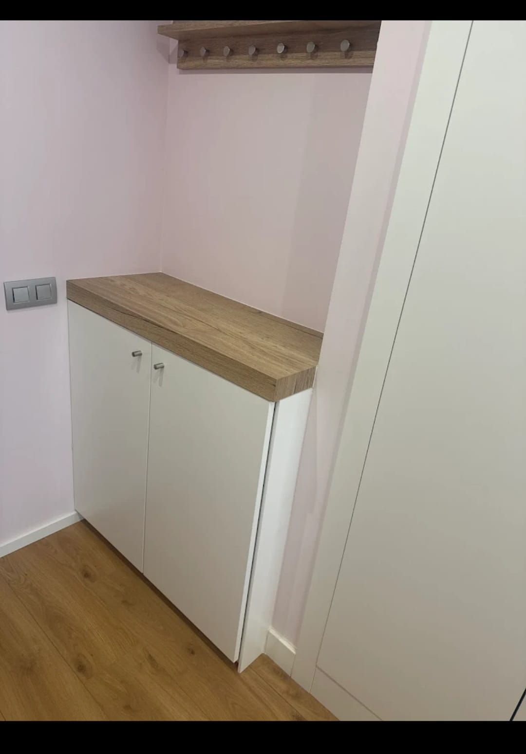 Armario blanco con encimera de madera contra una pared rosa. Suelo de madera.