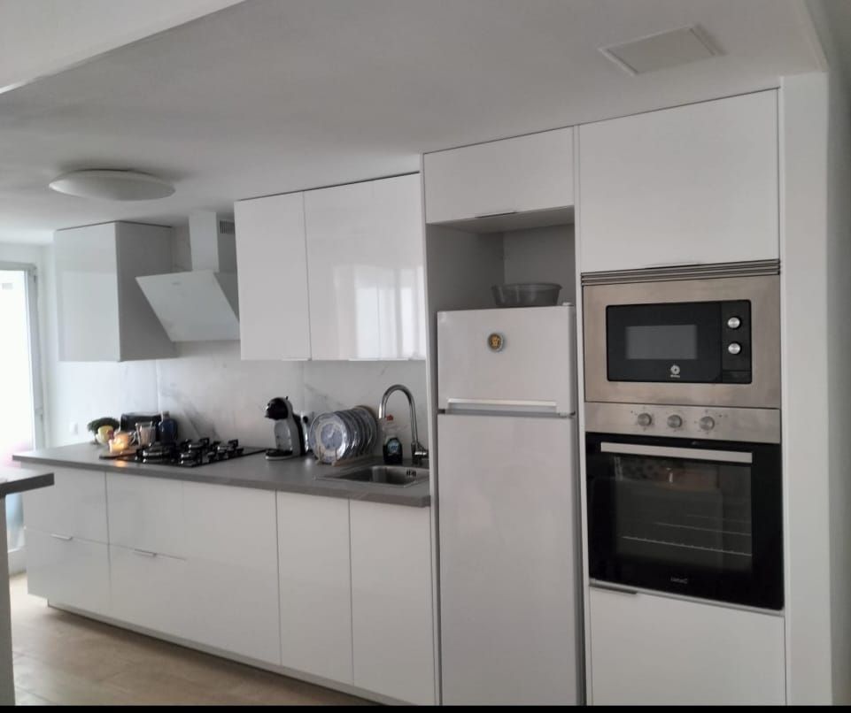 Cocina blanca con gabinetes, electrodomésticos y encimeras.