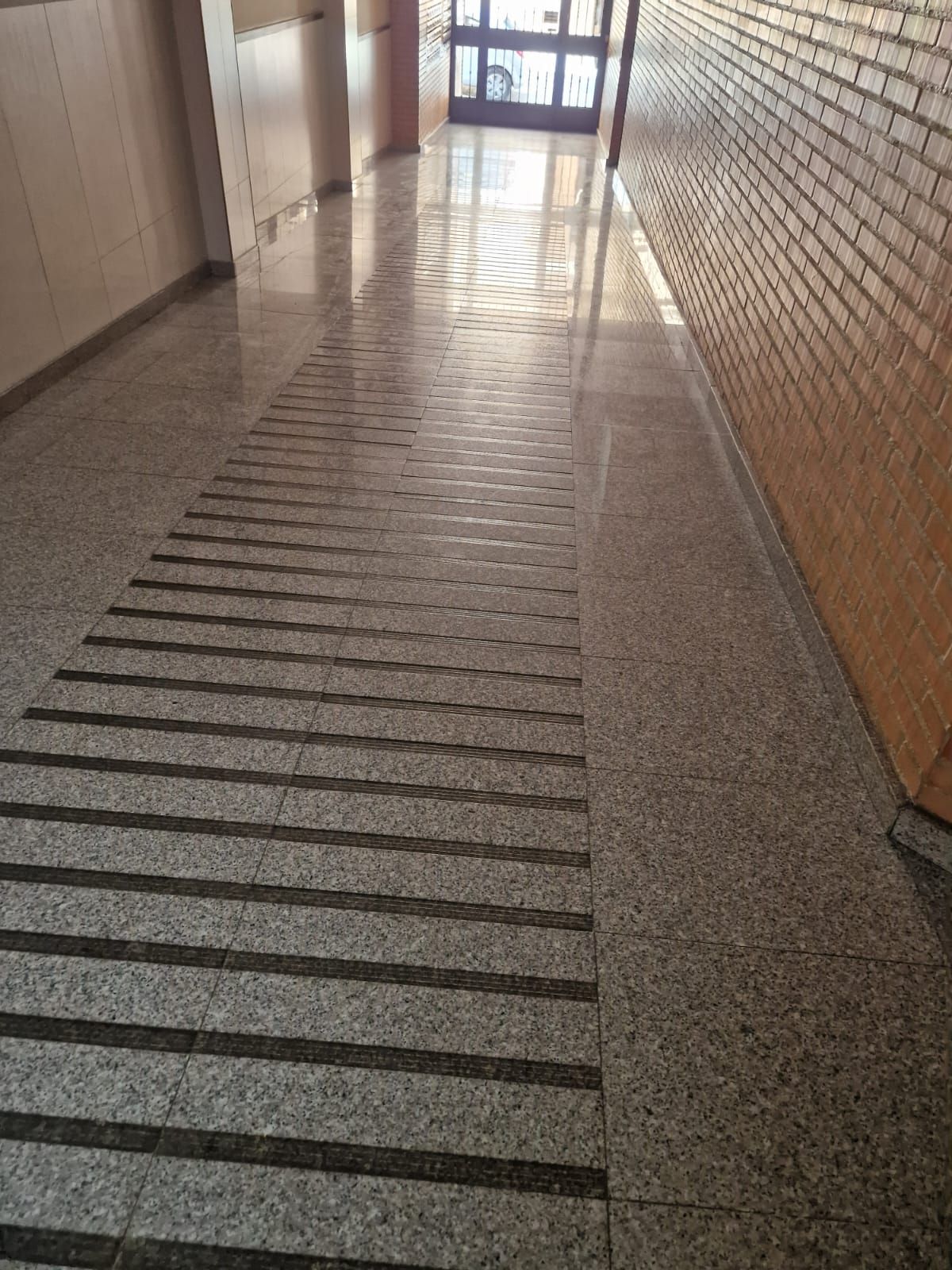 Pasillo con suelo moteado y pared de ladrillo, con una sección texturizada para mayor accesibilidad.