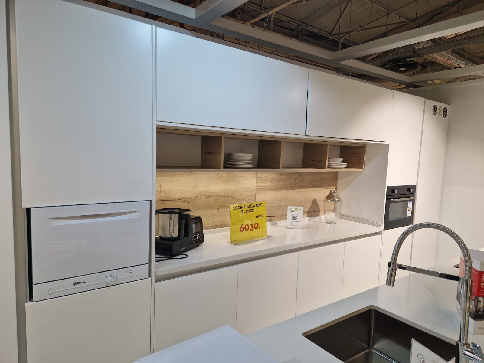 Cocina blanca moderna con electrodomésticos integrados, estantes abiertos y fregadero de acero inoxidable.