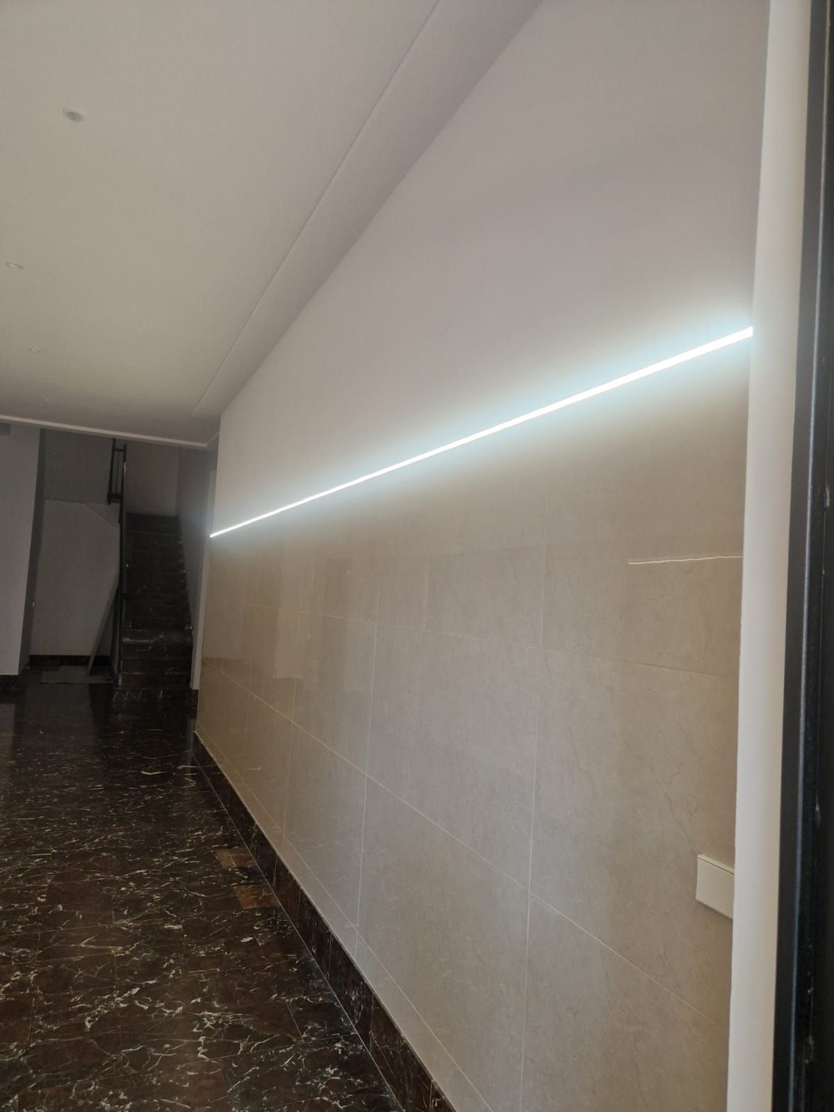 Pasillo largo con tira de luz LED blanca y pared de azulejos.