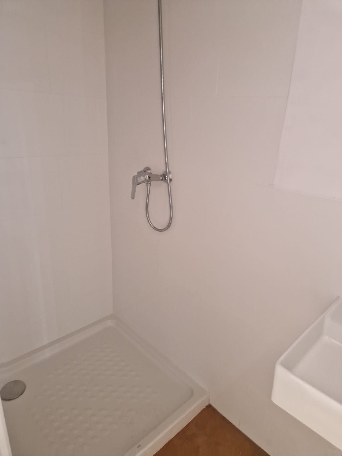 Pequeña ducha blanca con desagüe y grifo, junto a un lavabo blanco.