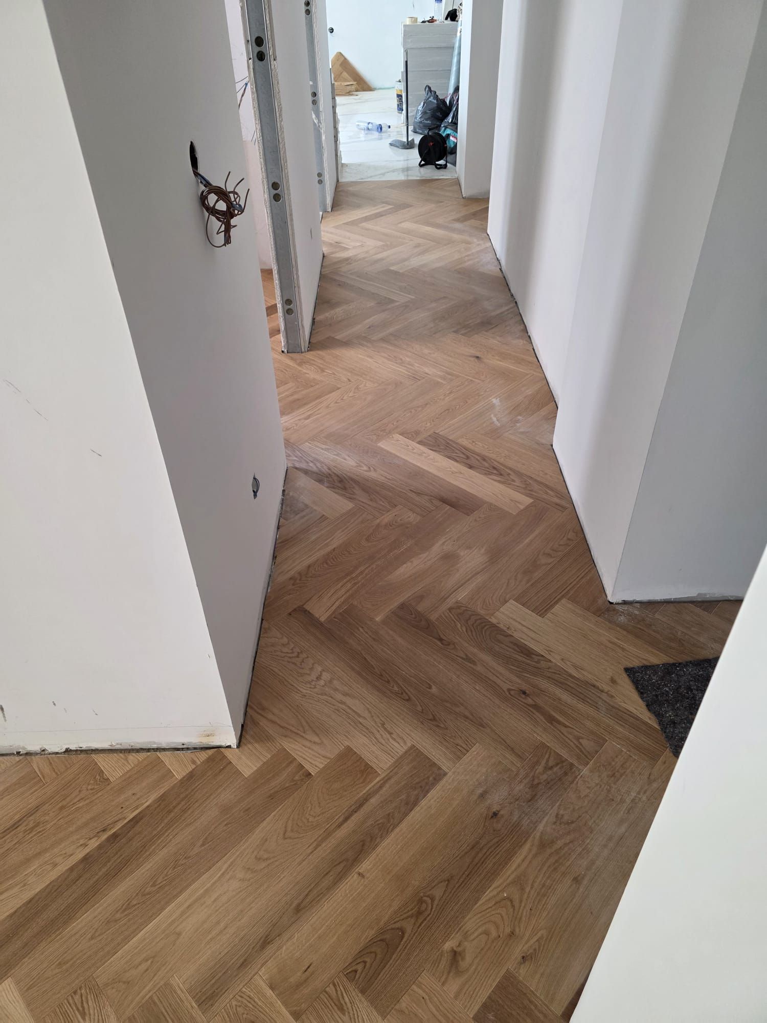 Pasillo con suelo de madera en espiga entre paredes blancas; construcción en progreso.