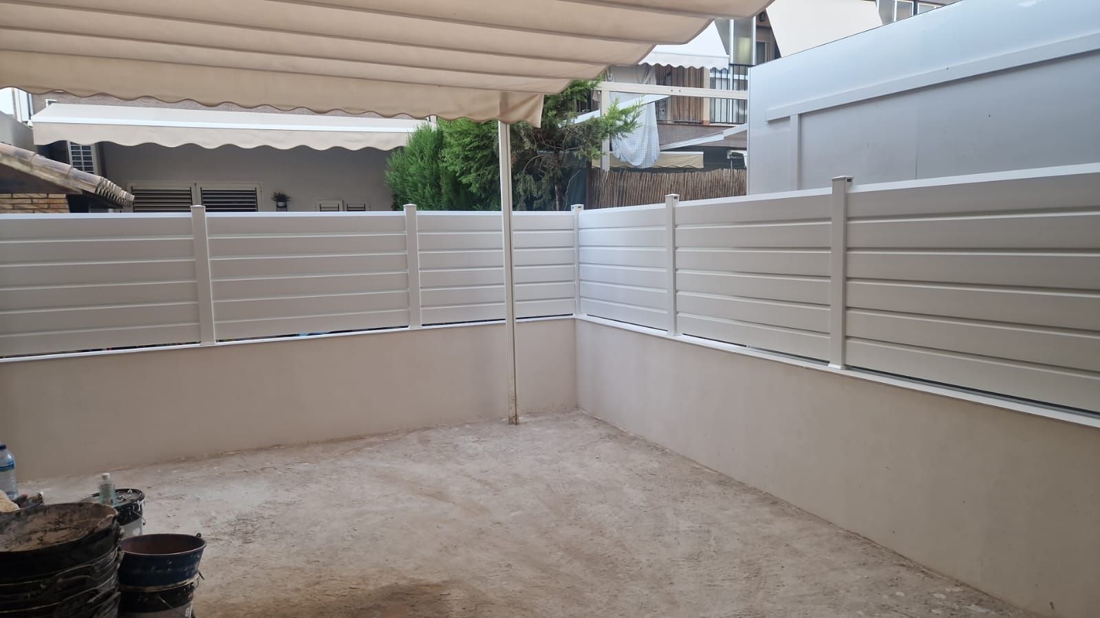 Patio vallado blanco con toldo beige.