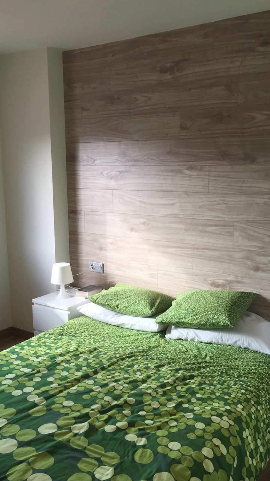 Un dormitorio con cama, mesita de noche, lámpara y pared de madera.