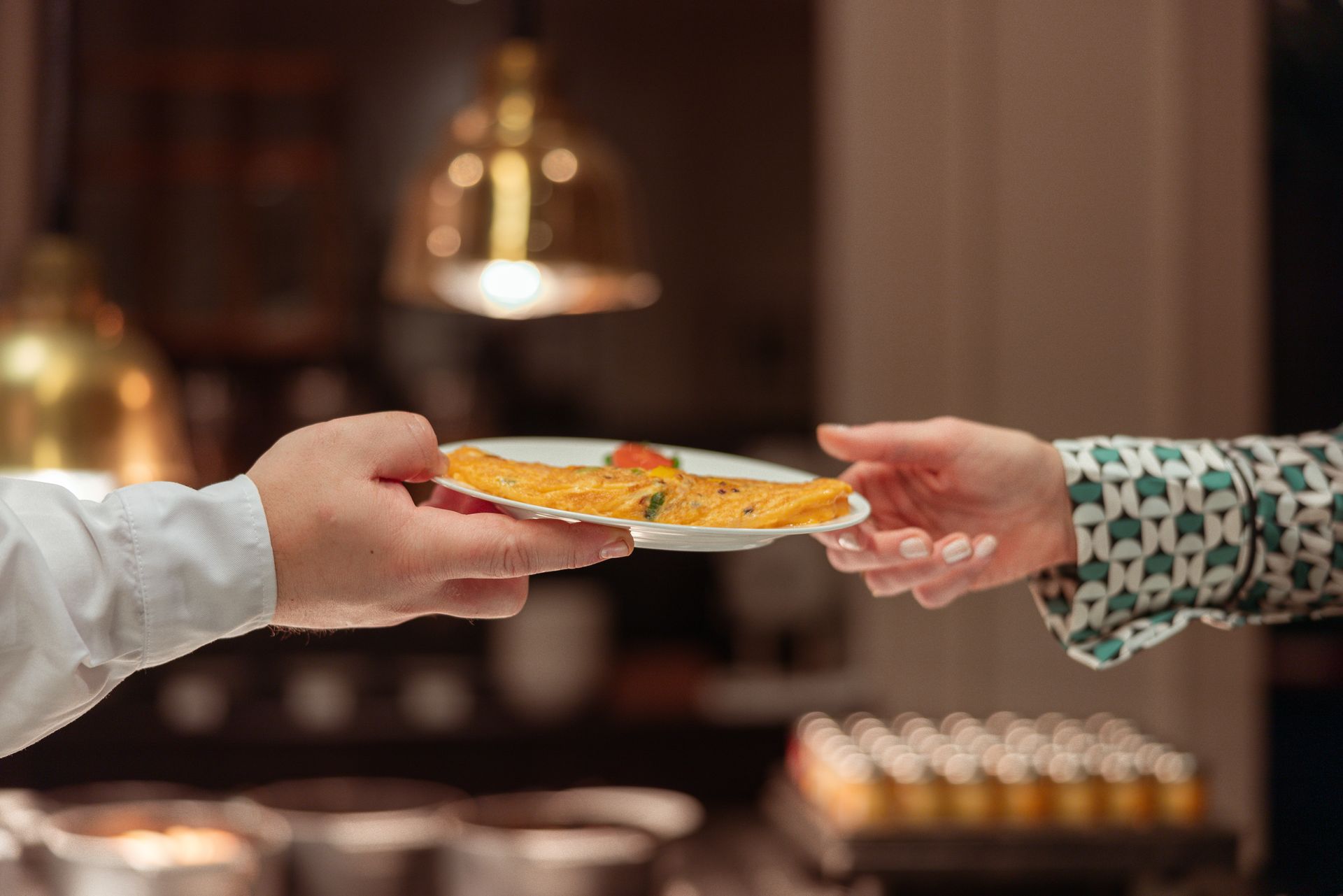 Twee handen met cocktails: in de ene een sinaasappelschil, in de andere een schijfje sinaasappel. Buiten. Proost!